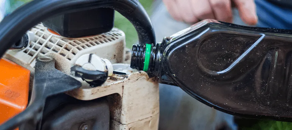 Una persona desconecta la línea de combustible de una cortadora de césped para drenar la gasolina vieja.