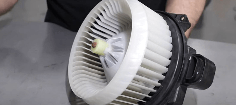 A close-up of a new white blower motor fan assembly, also known as a squirrel cage fan, ready for installation in a heavy equipment HVAC system.