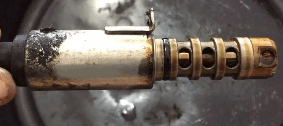 Close-up of a failed variable valve timing solenoid, covered in oil sludge and carbon buildup, showing a common reason for engine performance issues.