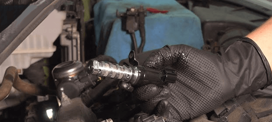 A mechanic carefully handles a clean VVT solenoid before installing it into a machine's engine, a key step in the repair process.