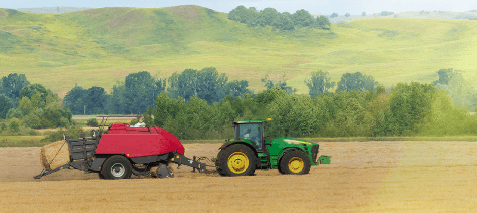 A powerful green tractor and red hay baler operate seamlessly in a vast, golden field under a bright sun, embodying the productivity of the 'Sunbelt' region. This scene highlights the essential agricultural machinery that FridayParts helps keep running.