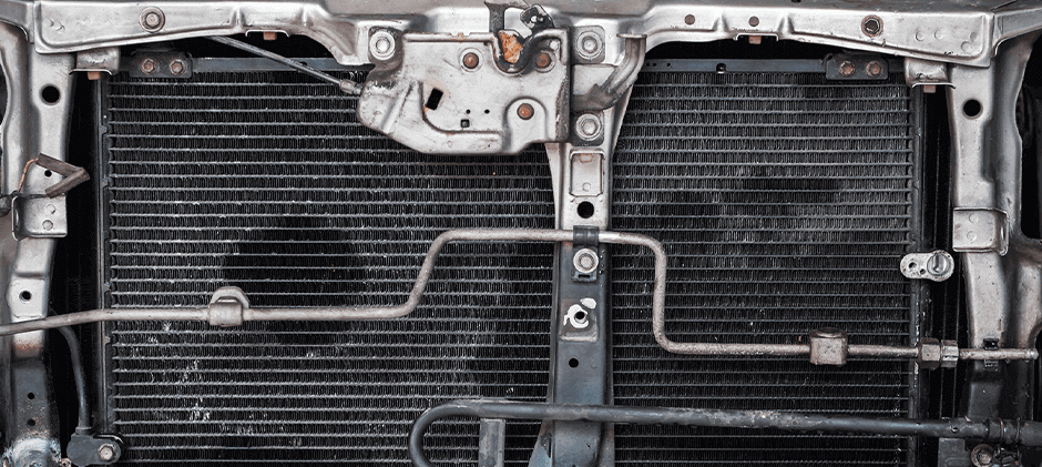 A close-up view of a radiator installed in the front of a heavy machine's engine bay that is leaking.
