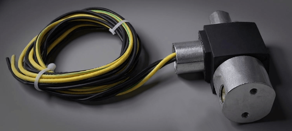 A 3-way solenoid valve with its black electrical coil and wiring, used to divert fluid flow between two different paths on farm or construction equipment.