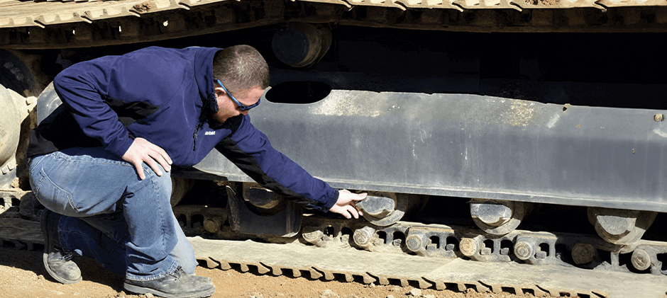 A man inspects an excavator undercarriage