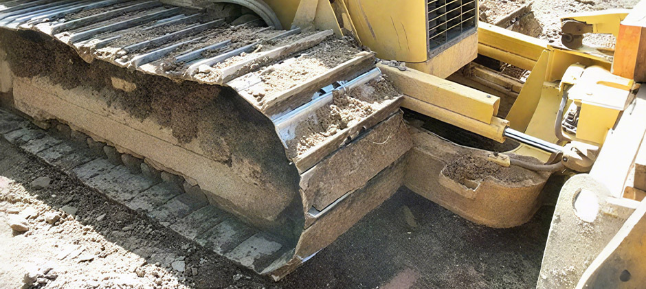 Close-up of a bulldozer track covered in dirt and soil, showing the harsh working conditions for undercarriage parts.