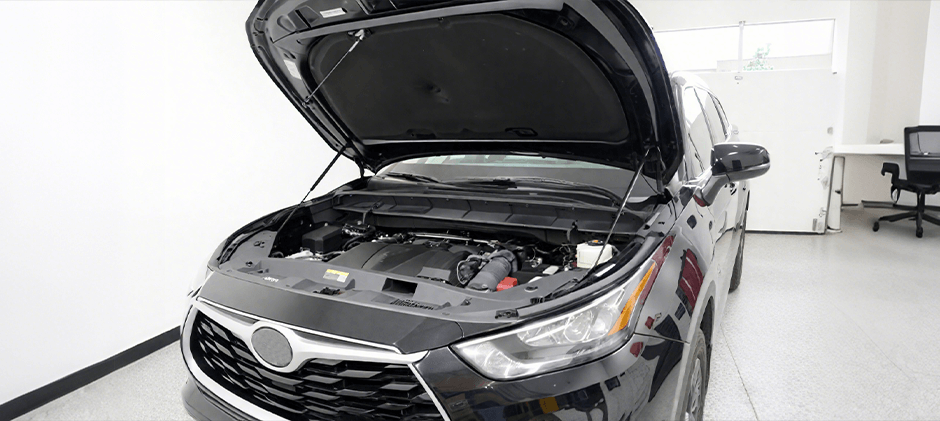 A black Toyota Highlander with its hood open in a workshop, showing the engine bay ready for diagnosis of a P1604 code.