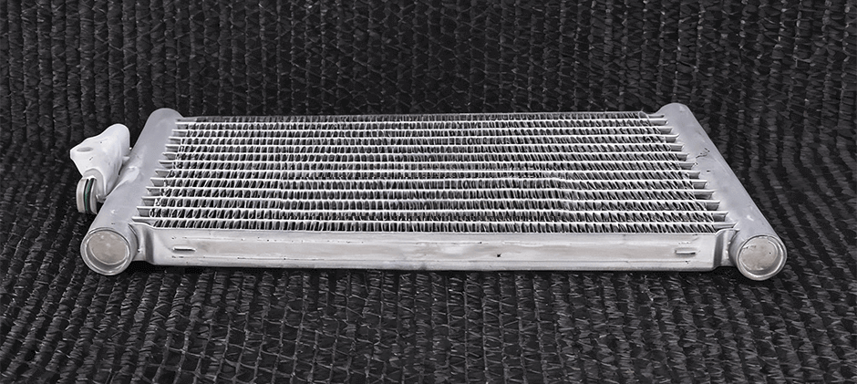 A close-up shot of a new, silver, air-cooled oil cooler with a plate-and-fin design, shown on a black background.