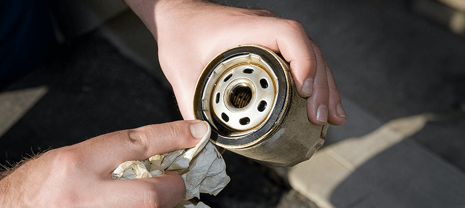 A person's hands wiping the rubber gasket of a used spin-on oil filter with a paper towel.