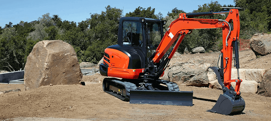 A Kubota KX040-4 conventional tail swing excavator with an enclosed cab, positioned on an open, rocky job site ready for heavy-duty work.