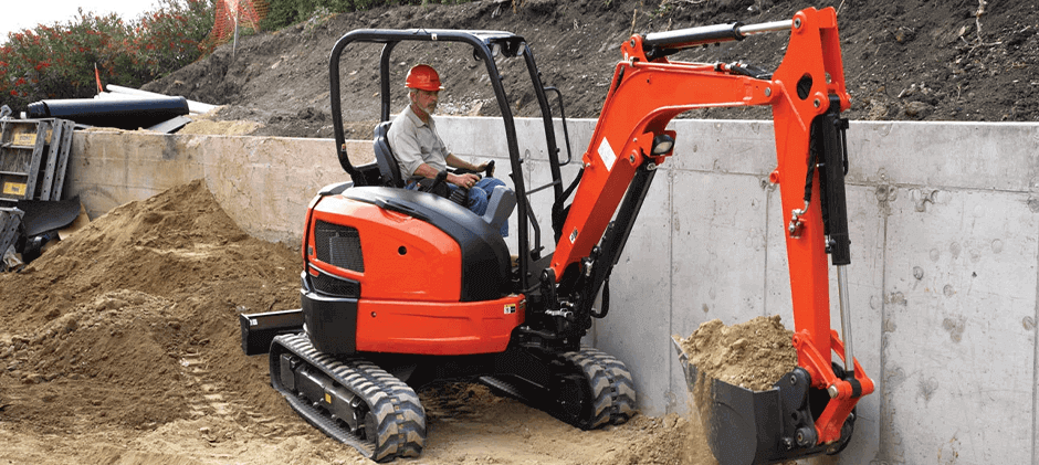 An operator digging with a Kubota U35-4 excavator in a tight space, demonstrating its zero-tail swing capability next to a concrete wall.