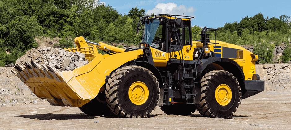 A yellow wheel loader carries a full bucket of rocks at a quarry, demonstrating its heavy-duty material handling capability.