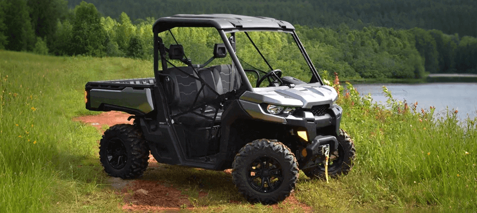  A green standard 2-door Can-Am Defender parked in a large, open grassy field.