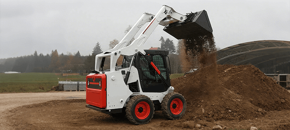 A white Bobcat skid steer loader dumps a bucketful of soil onto a large pile.