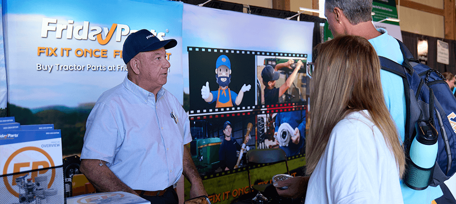 A FridayParts team member in a branded cap talks with two returning customers, the Johnsons, at the bustling Sunbelt AG Expo booth.