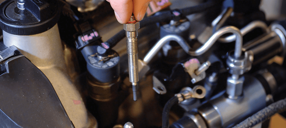 A close-up of a mechanic carefully installing a new glow plug into a diesel engine's cylinder head during a replacement.