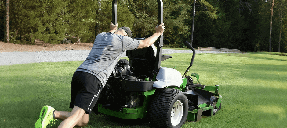 A man putting in effort to push a residential zero-turn mower across a lawn after disengaging its hydrostatic transmission to enable freewheel mode.