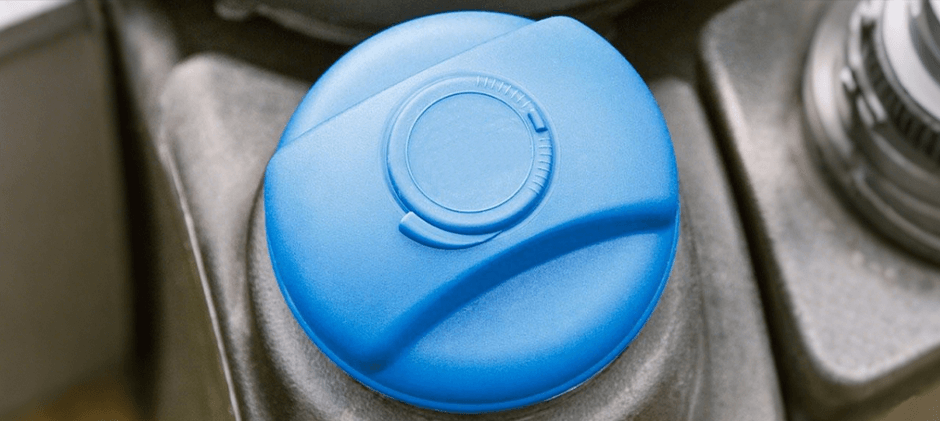 Close-up of a bright blue DEF (Diesel Exhaust Fluid) cap on a Kubota tractor engine.