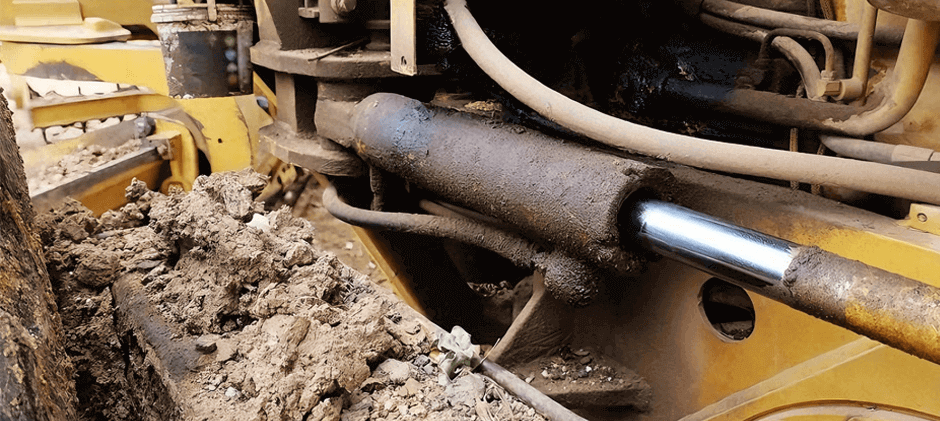 A hydraulic cylinder on a bulldozer covered in mud, showing the harsh working conditions that lead to hydraulic system contamination.