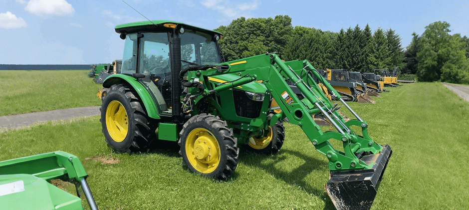 A cabbed John Deere 5065E tractor equipped with a front loader attachment, parked on a grassy area at a dealership or large property.