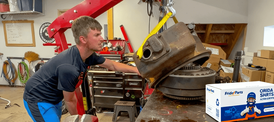 A mechanic using an engine hoist to lift a heavy equipment torque converter during a replacement in a workshop, with a FridayParts box visible.