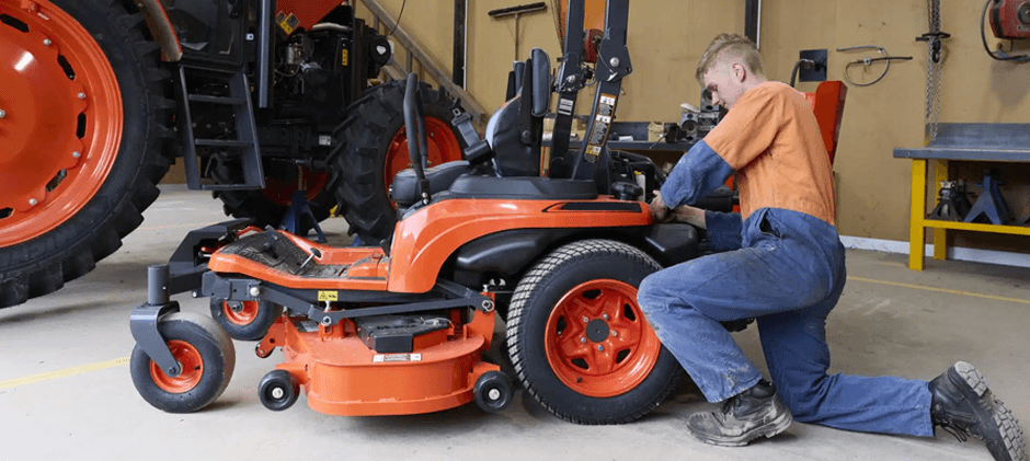 A mechanic performs maintenance on a Kubota zero-turn mower using aftermarket parts in a repair shop.