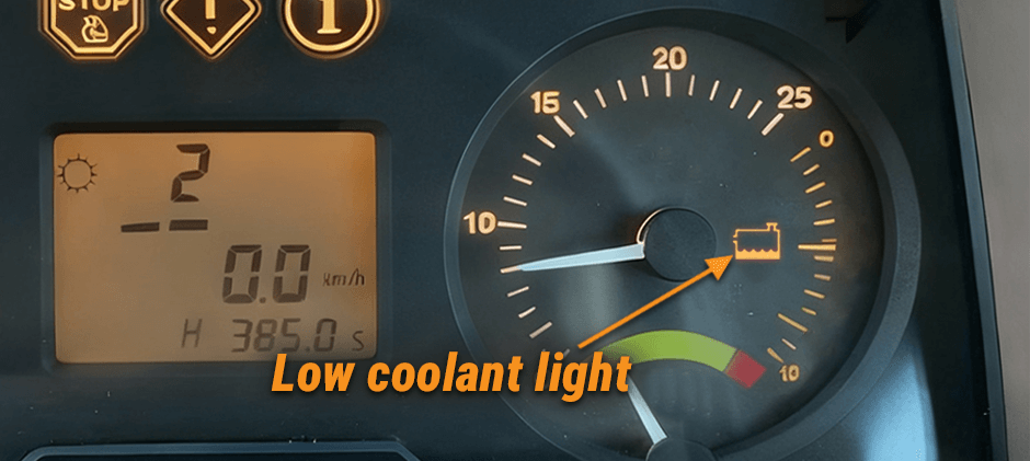 The low coolant warning light illuminated on a modern tractor's dashboard, which features both digital and analog gauges.