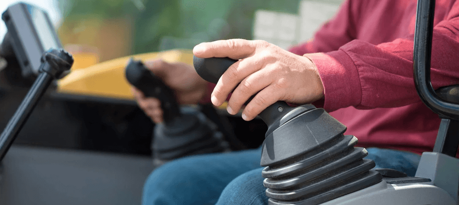 Close-up of an operator's hand holding and operating a joystick controller inside the cab of a piece of heavy machinery.