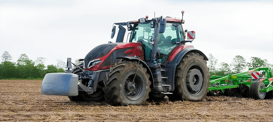A red heavy-duty tractor tilling a field with visibly underinflated tires, illustrating the hidden risk and performance loss when operating machinery with low pressure.