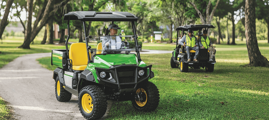 A Gator 4x2 utility vehicle driving on a smooth, paved path in a park-like setting.