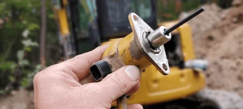 A mechanic's hand holding a faulty fuel shut-off solenoid removed from a piece of heavy equipment.