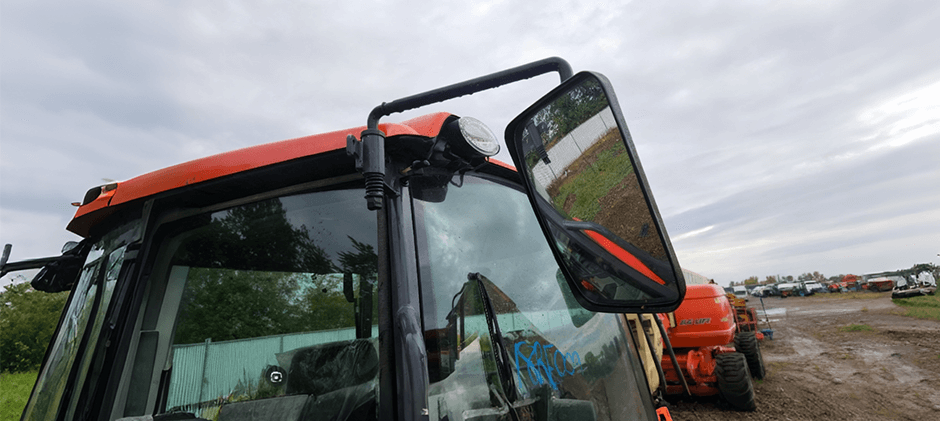 Close-up view of a rear view mirror assembly mounted on the cab of an orange construction machine.