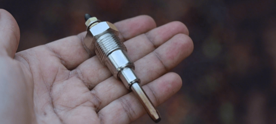 A person's hand holding a clean, new diesel engine glow plug, showing its metal body, threads, and smooth heating tip.