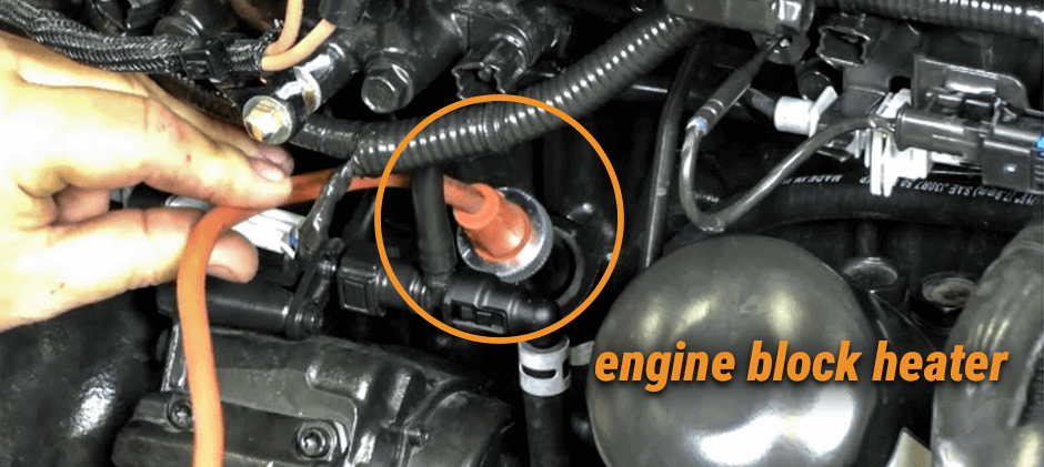 A hand plugging an extension cord into an engine block heater plug located in the engine bay of a machine.