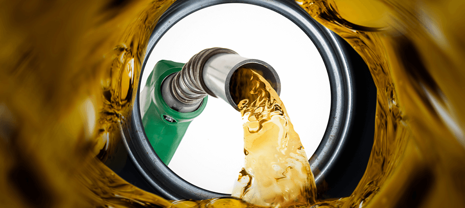 A close-up view from inside a tank as a green fuel nozzle pours clean, golden diesel fuel.