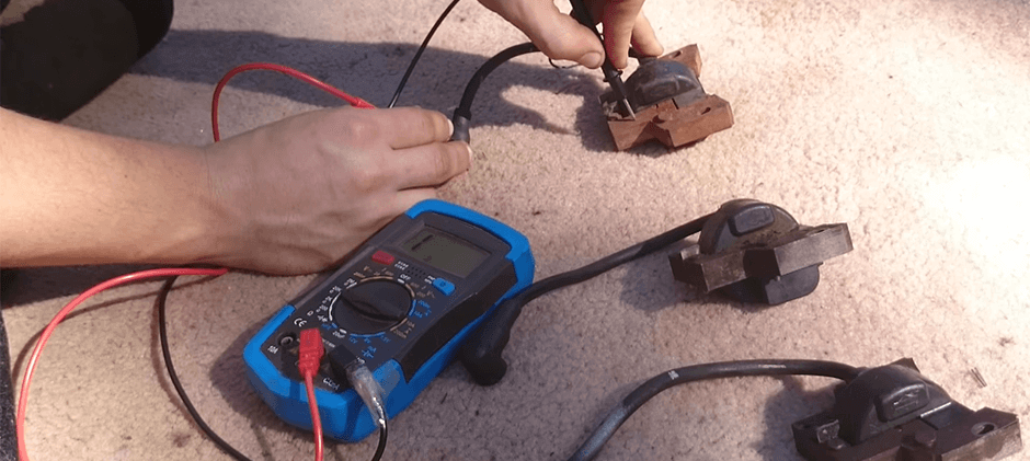 Hands using multimeter probes to check the resistance on one of several canister-style ignition coils laid out for testing.