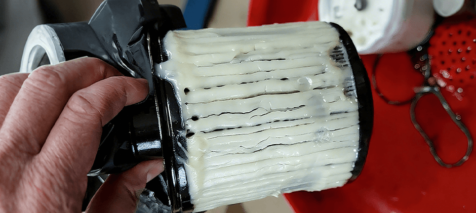 A hand holds a diesel fuel filter that is completely clogged with thick, white paraffin wax from gelled fuel.