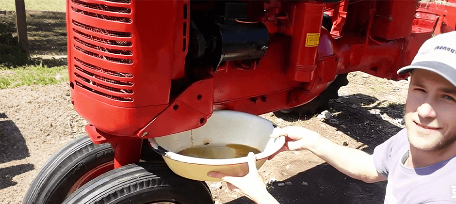An animation showing rusty, brown, and contaminated coolant being drained from an old red tractor's cooling system into a white bowl.