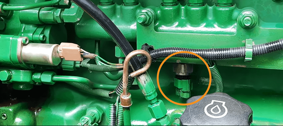 The location of a fuel rail pressure sensor on a John Deere engine, circled in orange to show where it's installed on the fuel rail.