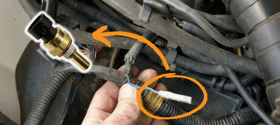 A hand holding the electrical connector for a coolant temperature sensor in an engine bay, with an arrow pointing to its location.