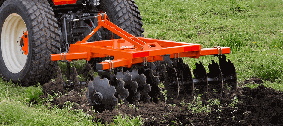 An orange disc plow attached to a tractor cutting through and turning over sod in a green field.