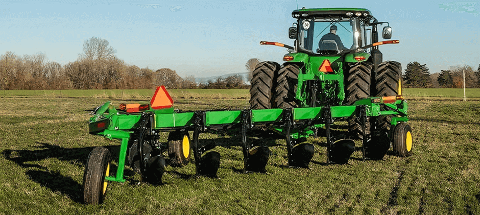 A large green tractor with a multi-bottom moldboard plow attached, sitting in a field.