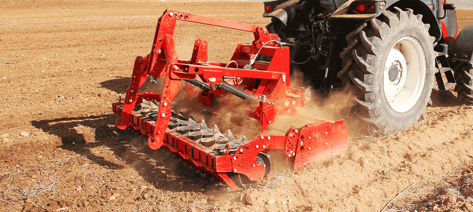 A red rotary tiller pulverizing dry soil, kicking up a cloud of dust as it prepares a fine seedbed.