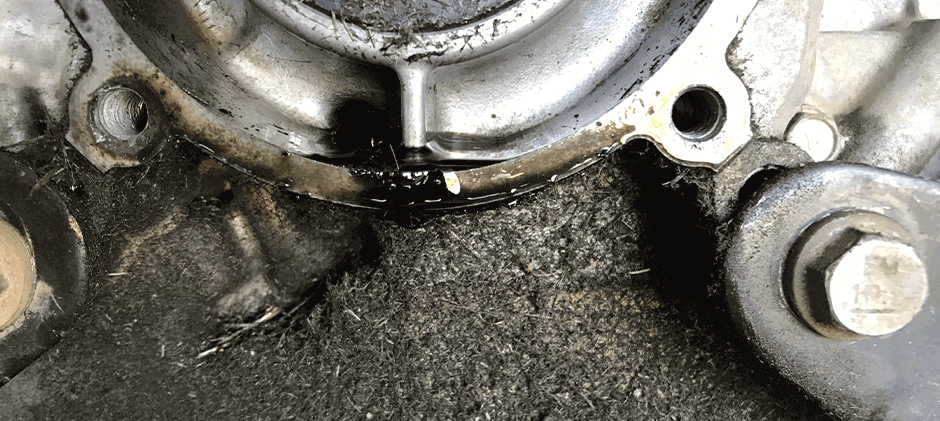 A macro shot showing fresh engine oil actively seeping from a failed crankshaft seal onto a dirty engine block.