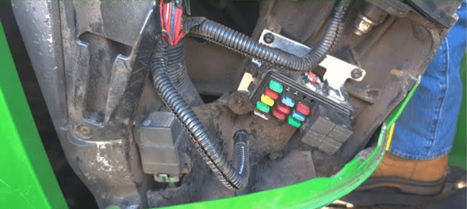 A wider view showing the location of a fuse and relay panel tucked into the side of a green piece of off-road machinery, surrounded by wiring harnesses.