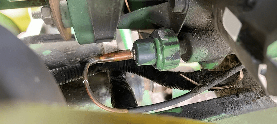 A close-up of an oil pressure sensor installed on a dirty engine block, with its electrical connector and wiring visible.