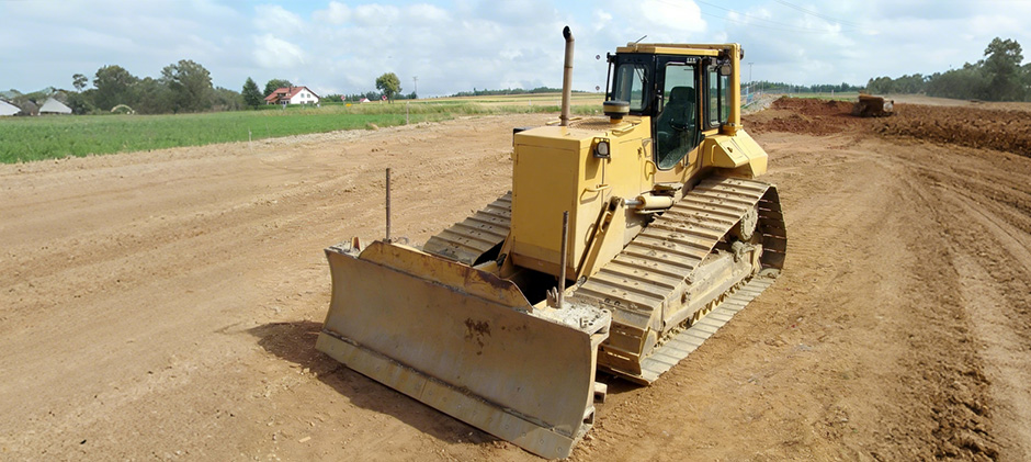A yellow bulldozer with a large front blade leveling a dirt path on a construction site.