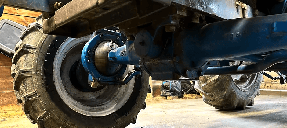 A low-angle close-up view of a tractor's heavy-duty front axle housing connected to a large, rugged tire.
