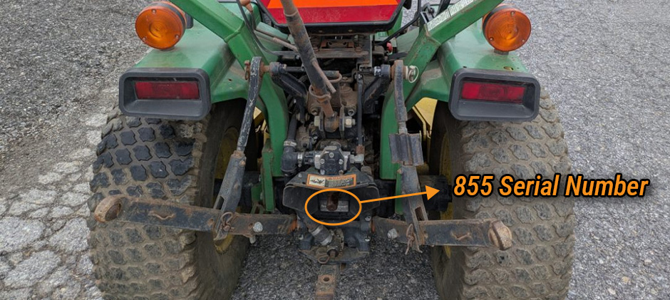 Close-up of the rear of a John Deere 855 tractor with an arrow pointing to the serial number plate below the PTO shaft.