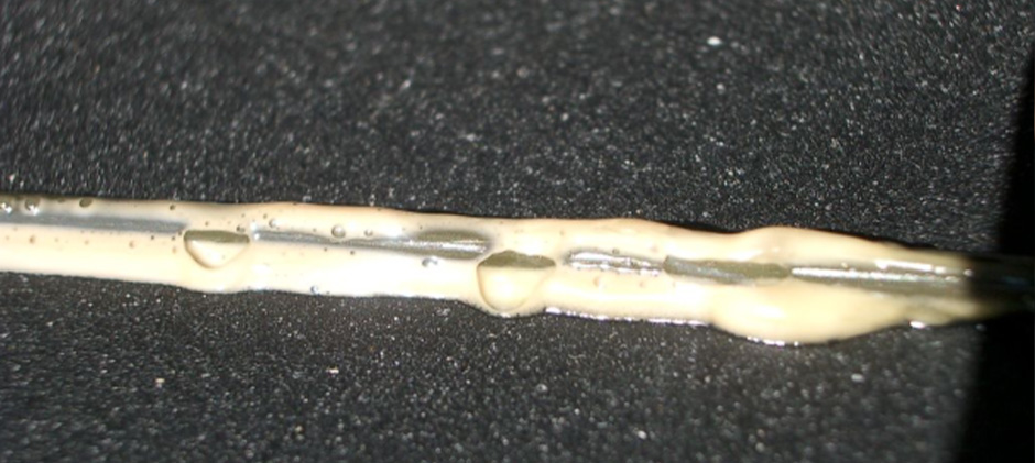 Symptom of Water Contamination in Oil Close-up of a dipstick coated with thick, milky, and foamy engine oil, indicating water contamination.