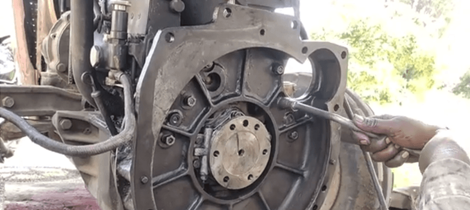 A mechanic uses a long wrench to work on the exposed clutch assembly of a heavy machine that has been split apart for the repair.